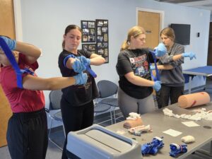 Four young women in a recent SORS Stop the Bleed training practice putting tourniquets on themselves and each other.